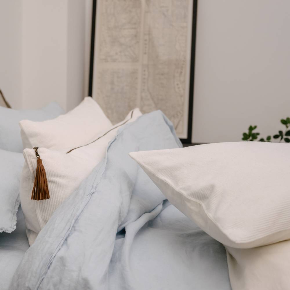 Light blue bedding and pillows on a bed with a neutral headboard.