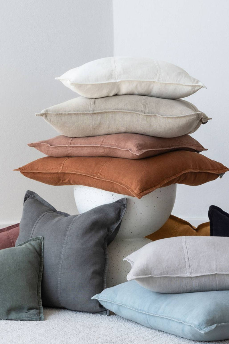 Stack of multicolored Eadie Lifestyle linen cushions against a light white background