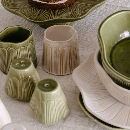 Collection of ceramic kitchen items including pots, bowls, and a salt and pepper shaker on a textured surface.