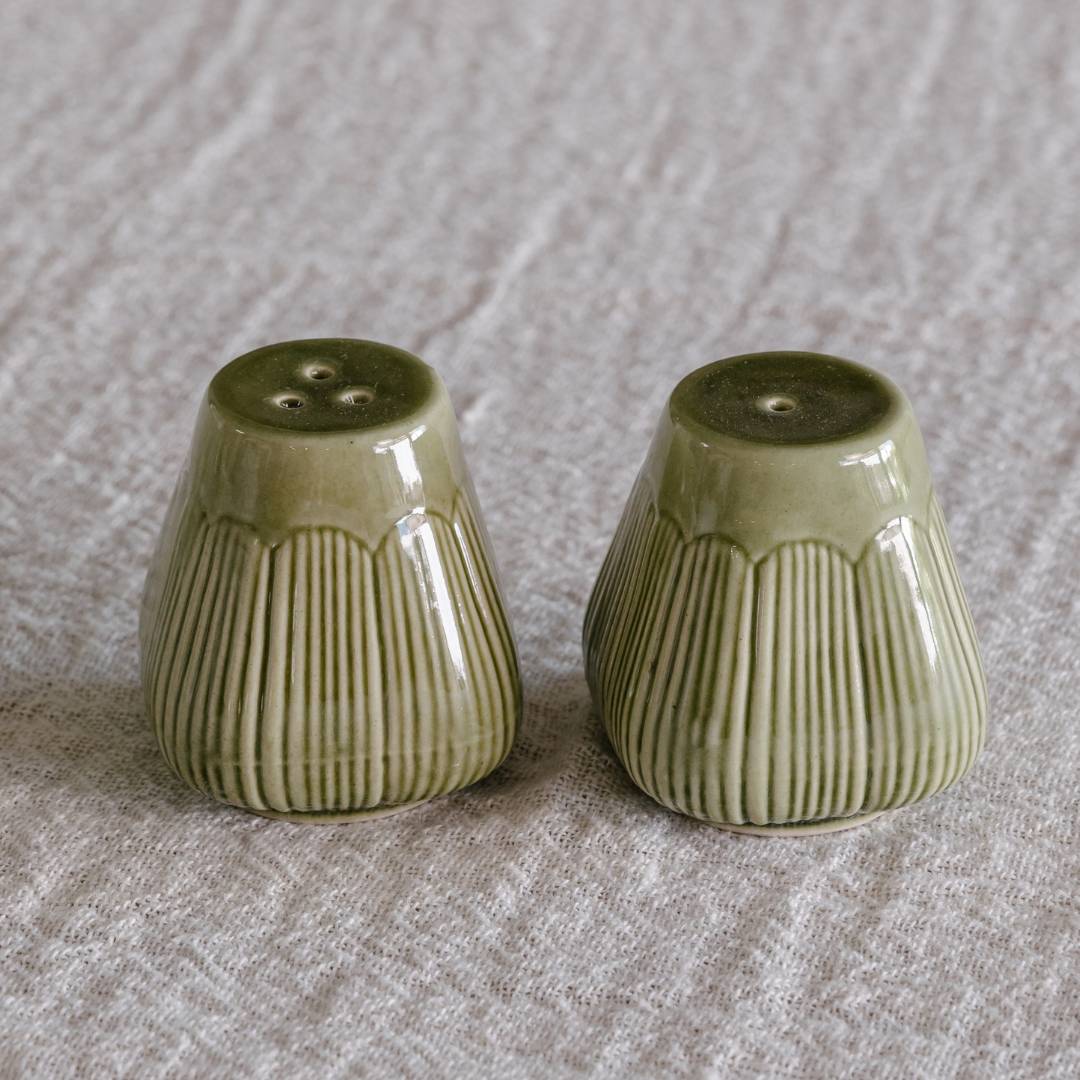 Two green ceramic salt and pepper shakers on a textured surface