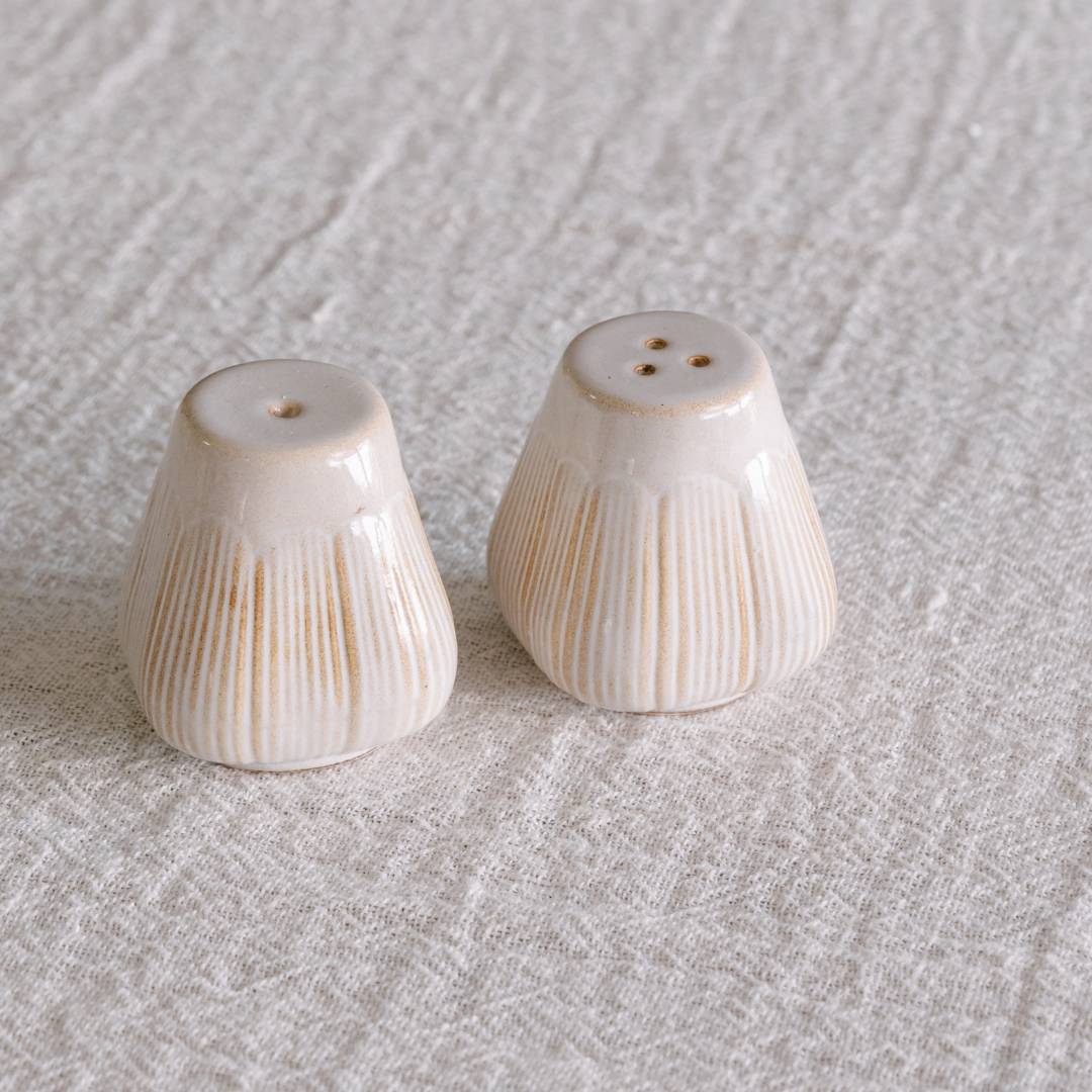 Two ceramic salt and pepper shakers on a textured beige surface