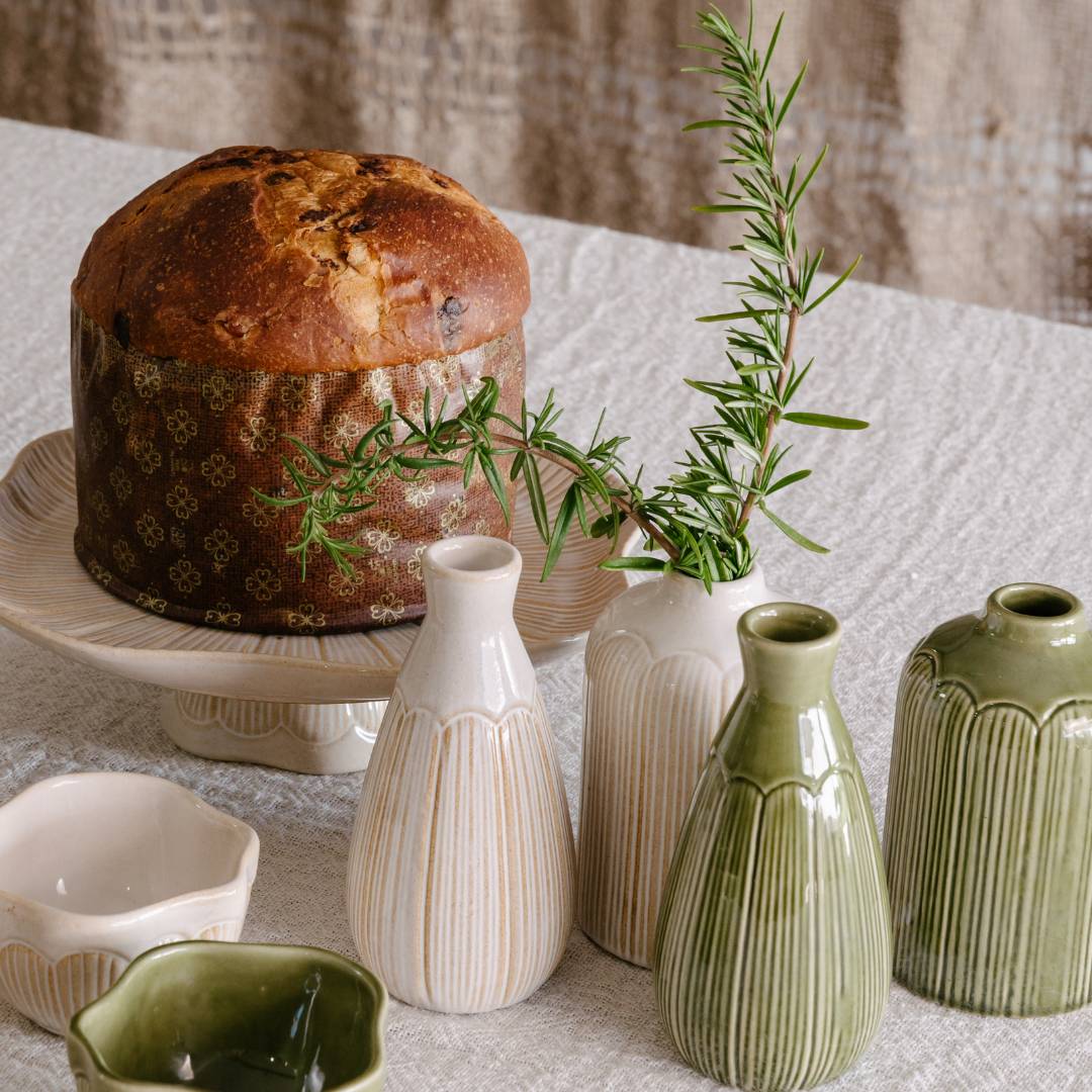 Baked bread loaf with greenery on a textured surface with ceramic vases.