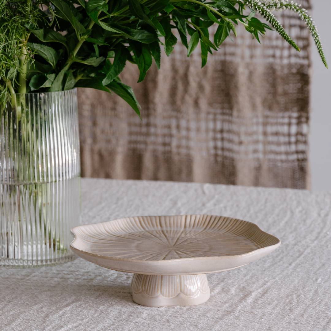 Decorative ceramic plate on a textured surface with a vase of greenery in the background.