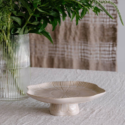 Decorative ceramic plate on a textured surface with a vase of greenery in the background.