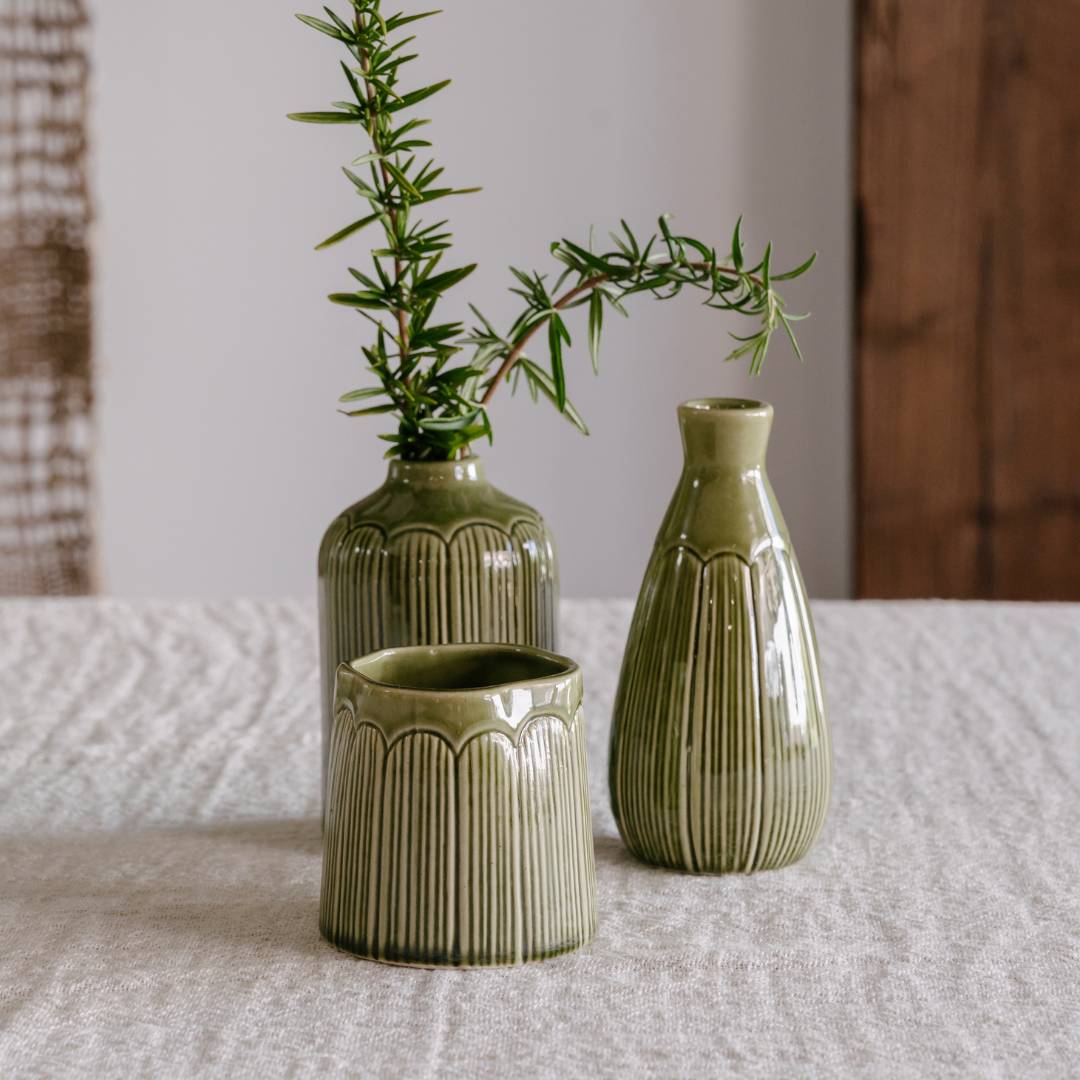 Three green ceramic vases with textured design on a textured surface.