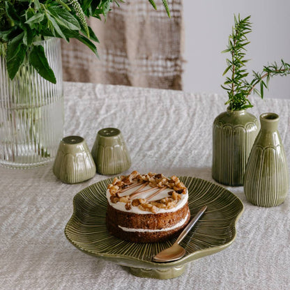Small cake on a decorative plate with green ceramic vases and plants in the background.