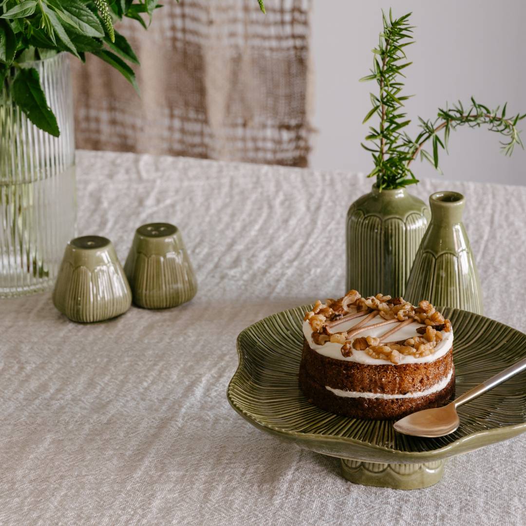 Small cake on a green plate with decorative vases and plants on a textured surface
