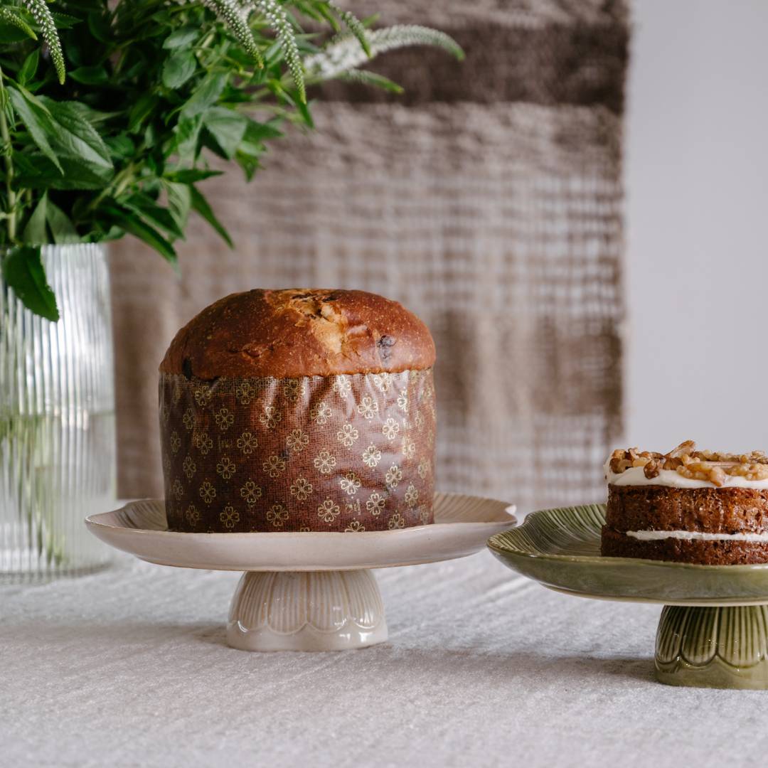 Baked loaf on a white cake stand with a small decorated cake on a green stand, against a neutral background.