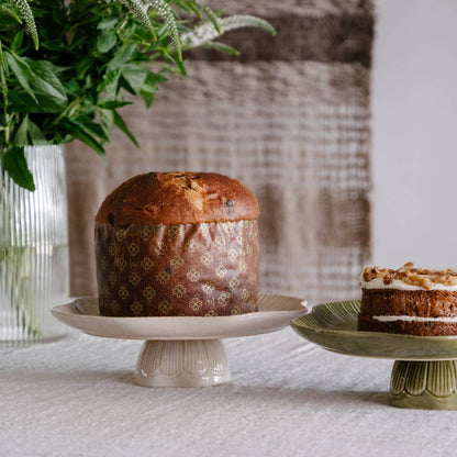 Baked loaf on a white cake stand with a small decorated cake on a green stand, against a neutral background.