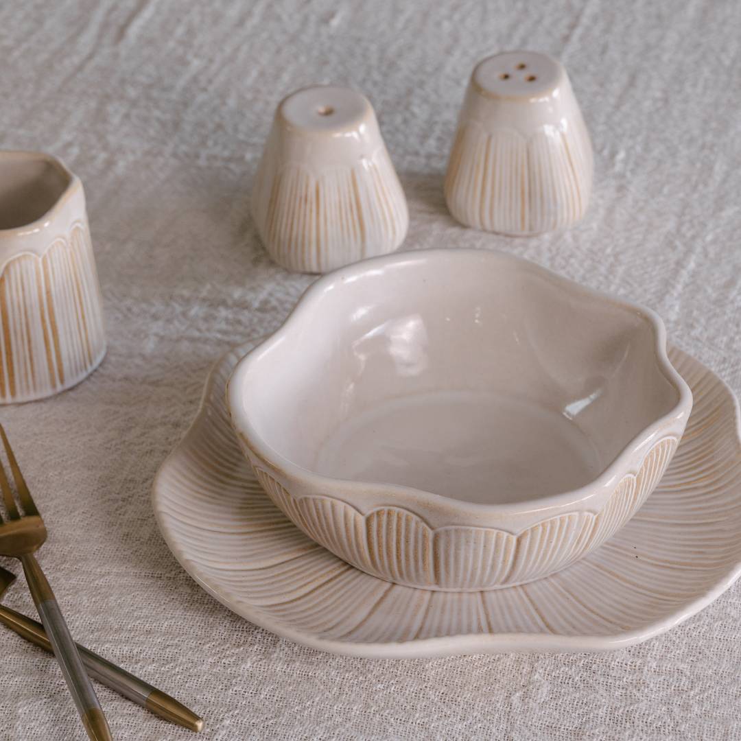 Ceramic bowl and salt and pepper shakers on a textured surface with gold forks.