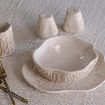 Ceramic bowl and salt and pepper shakers on a textured surface with gold forks.
