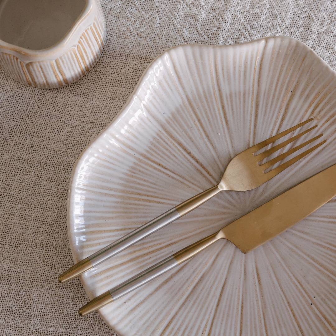 Gold fork and knife on a textured beige plate with a neutral background