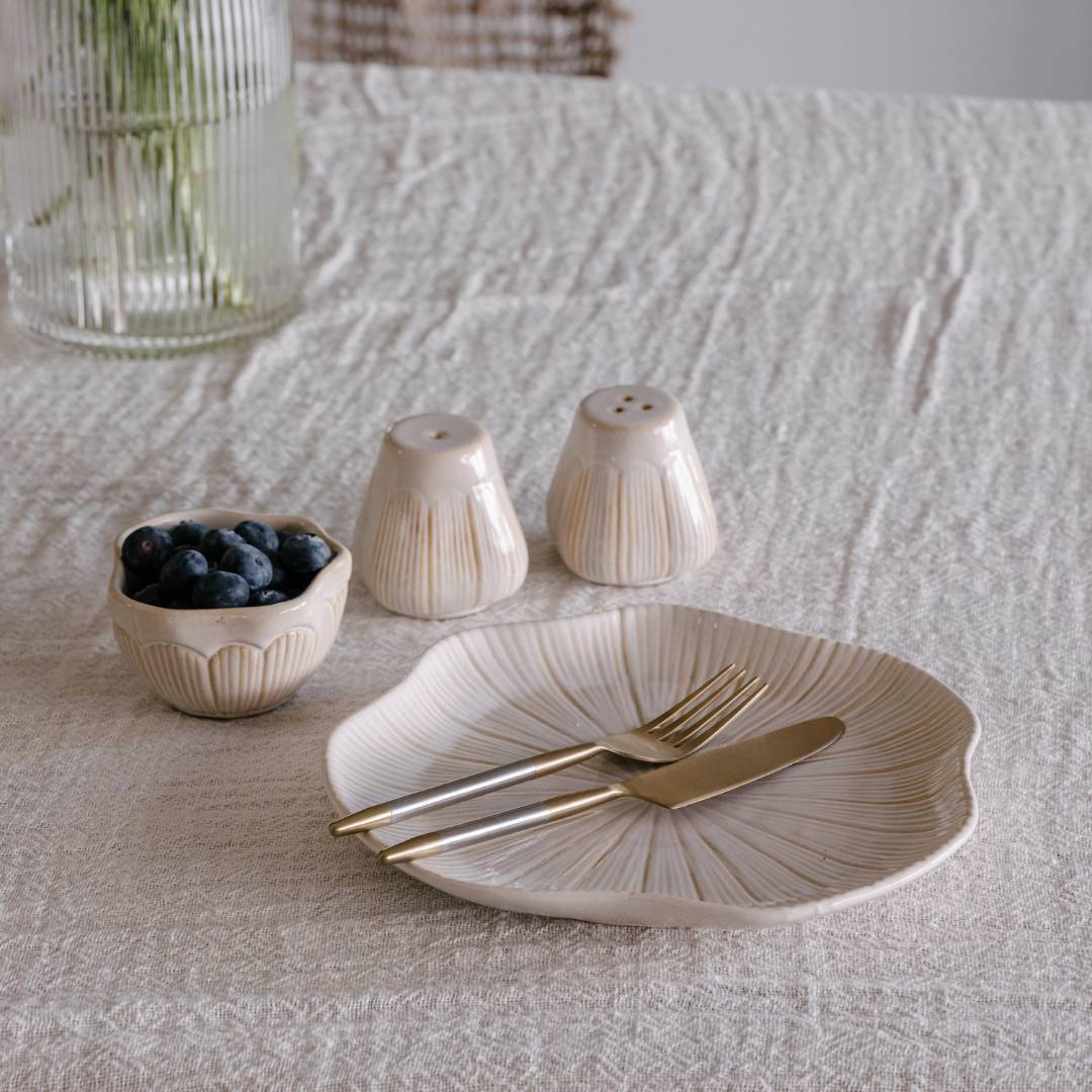 Ceramic tableware set with a plate, fork, knife, and small bowl on a textured surface.