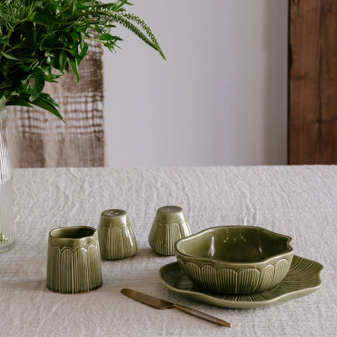 Green ceramic tableware set on a white tablecloth with a plant in the background.