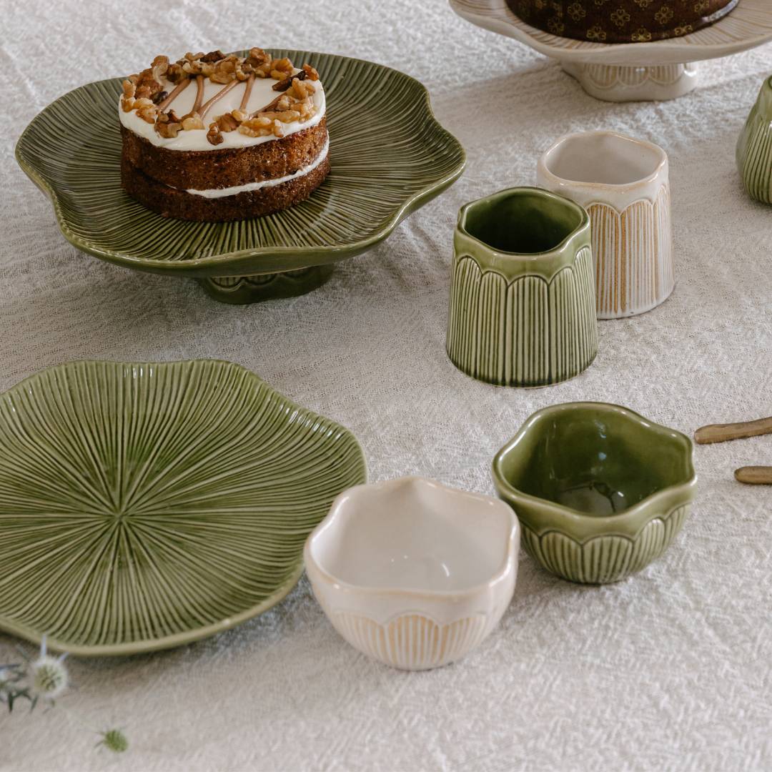 Green ceramic plates and bowls on a textured surface with a cake in the background.
