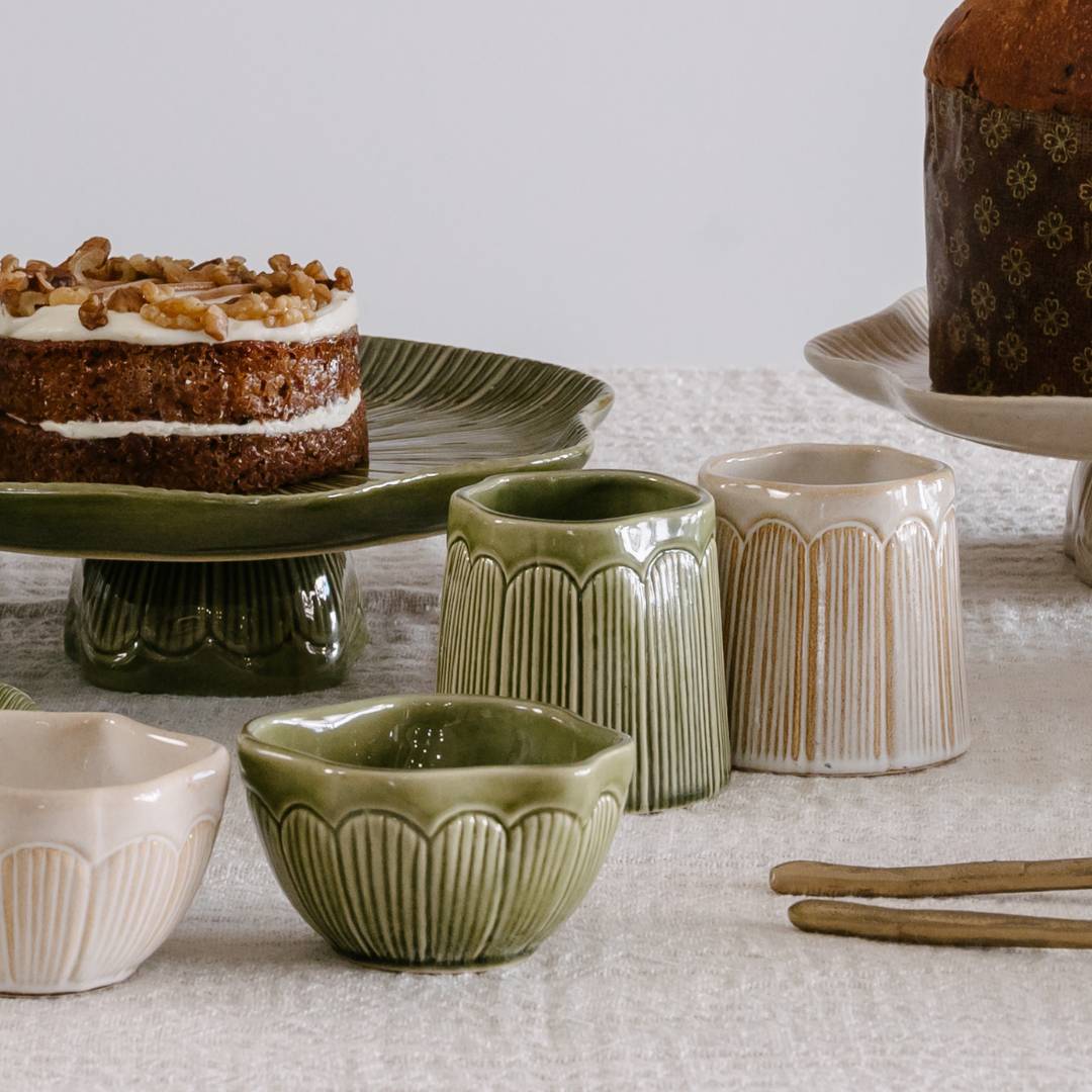 Ceramic bowls and containers on a textured surface with cakes in the background