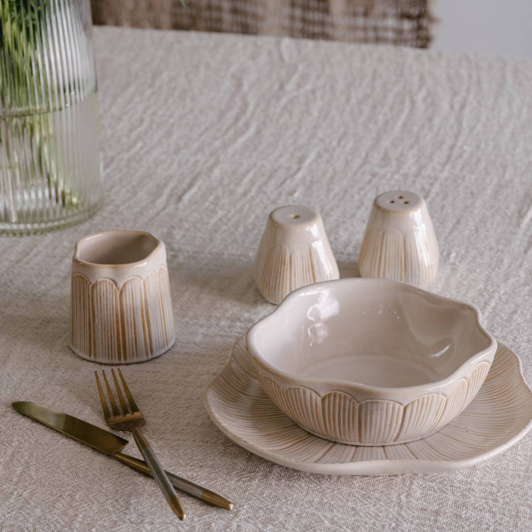 Ceramic tableware set including a bowl, plates, and cutlery on a textured surface.