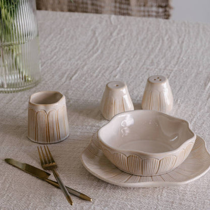 Ceramic tableware set including a bowl, plates, and cutlery on a textured surface.