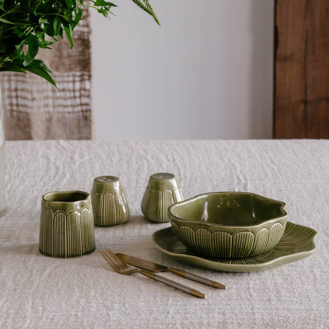 Green ceramic tableware set on a textured white surface with a plant in the corner.