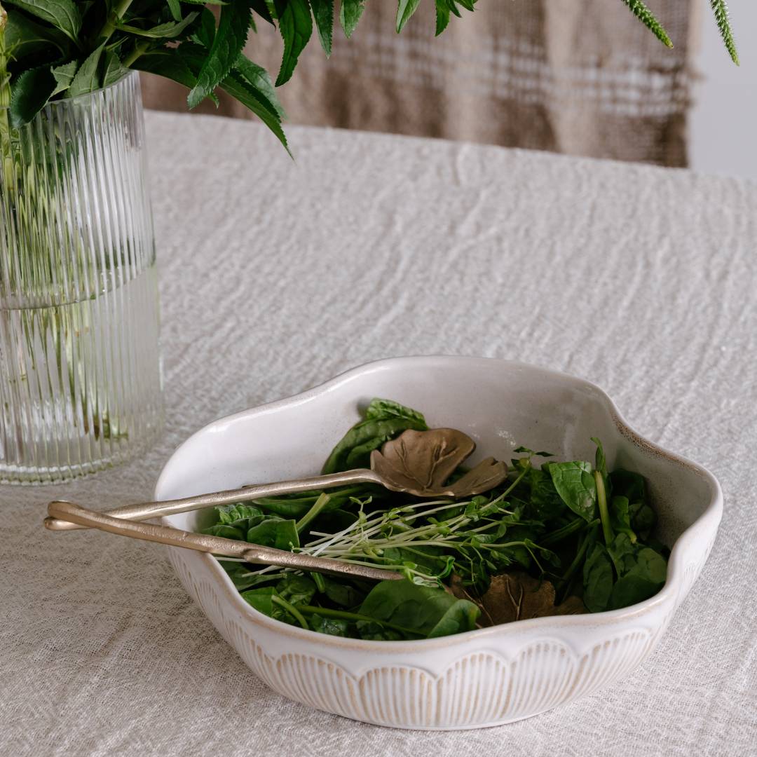 White bowl with green salad on a textured surface with a vase of flowers in the background