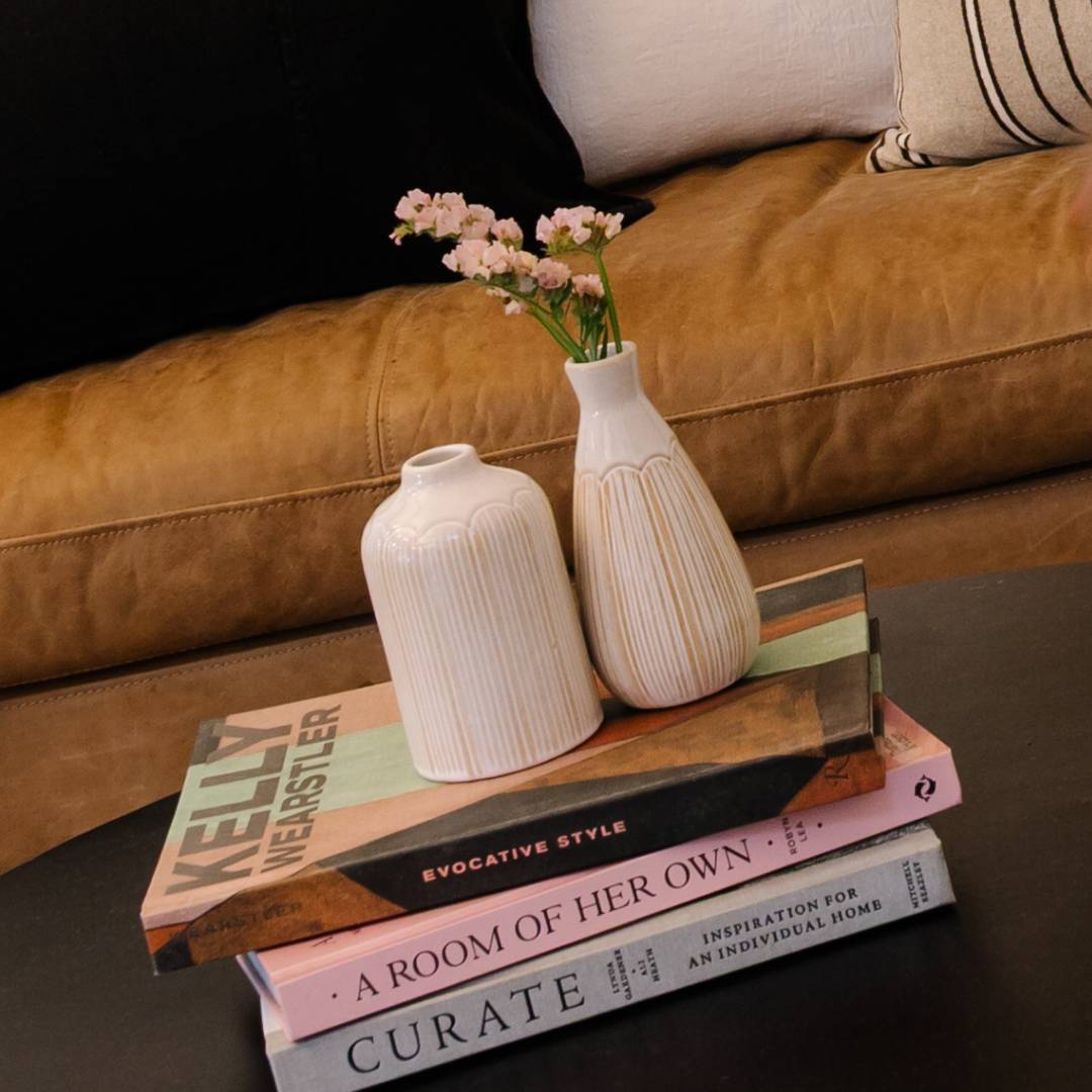 Stack of books with decorative vases on a coffee table in front of a brown sofa.