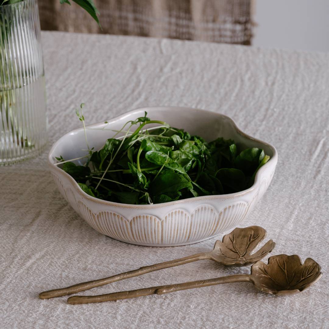 White ceramic bowl with green leaves on a textured surface with leaf-shaped spoons.
