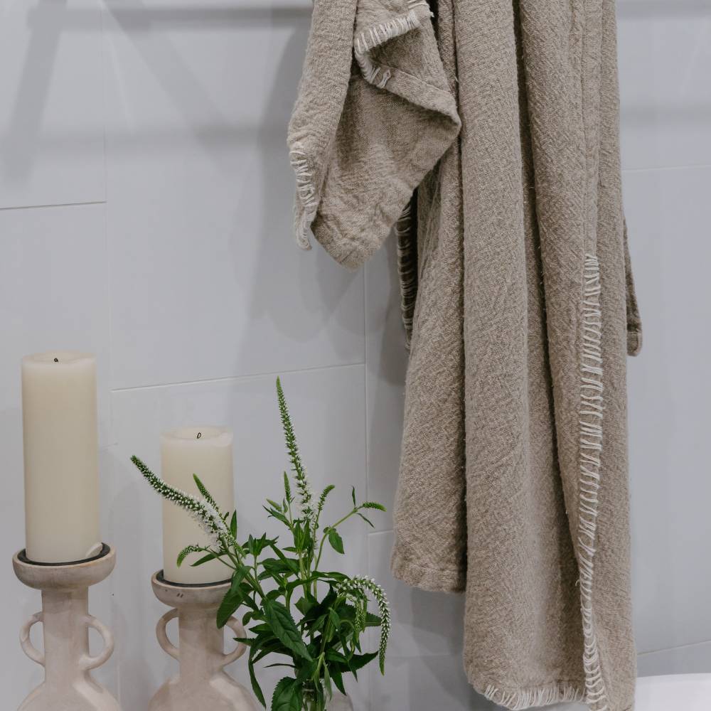 Beige bathrobe hanging on a hook with candles and a plant in the foreground.