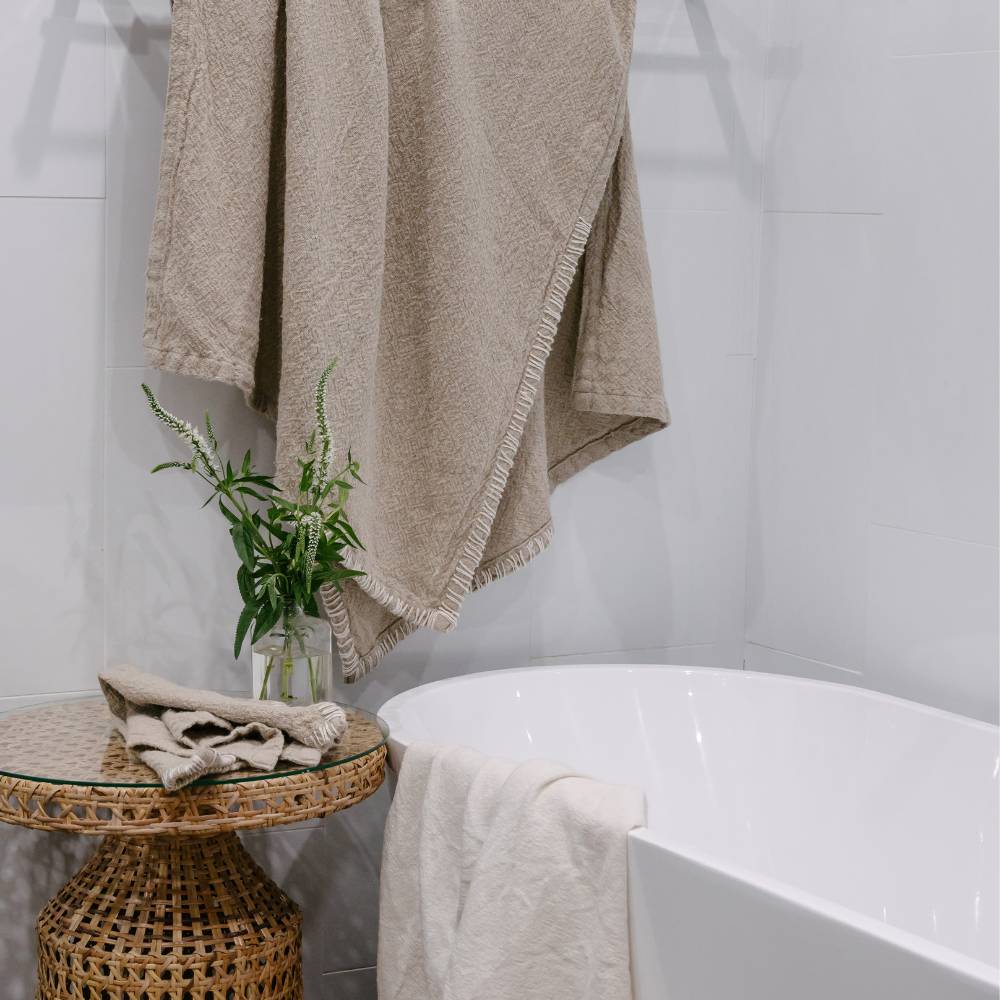 Beige towel draped over a white bathtub with a small table and plant in the foreground.