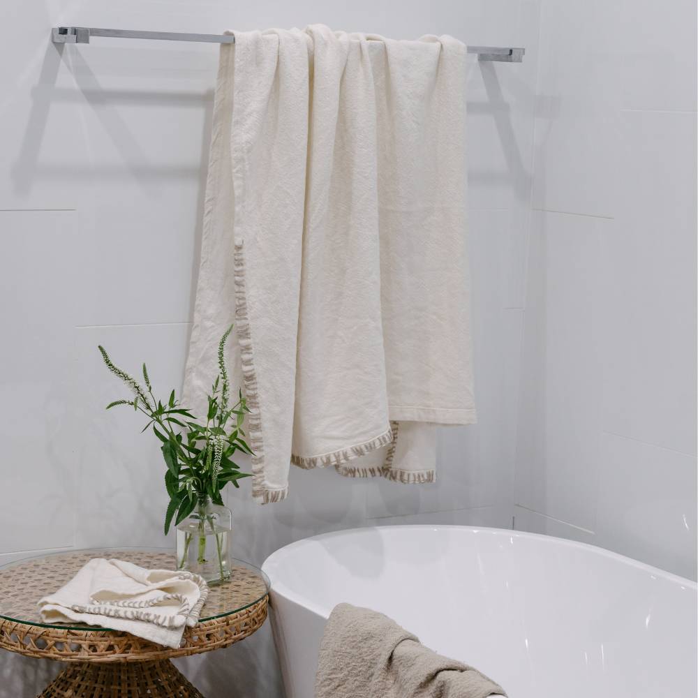 Beige towel draped over a towel rack in a bathroom setting with a plant and small table.
