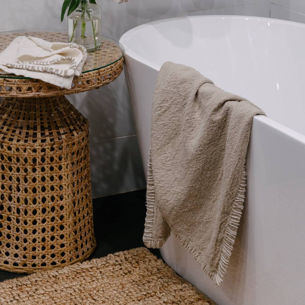 Bathroom scene with a white bathtub, beige towel, and wicker stool.